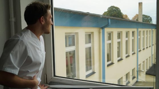 Pflegekraft hält sich de Bauch und schaut aus dem Krankenhausfenster